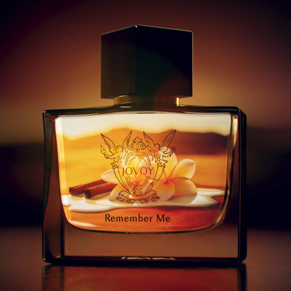 Jovoy - Remember Me Parfumflakon mit warmem Bernsteinlicht, verschnörkeltem Emblem und schwarzem Verschluss vor dunklem Hintergrund